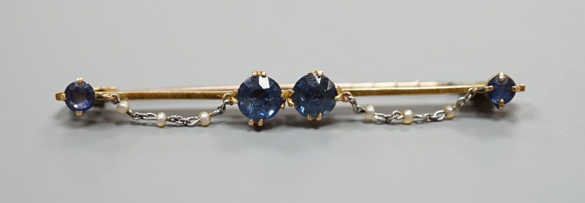 An early 20th century yellow metal sapphire and seed pearl set bar brooch, 61mm, gross weight 5.6 grams.